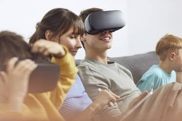 Happy family sitting on couch, using VR goggles and mobile devices - MCF00225