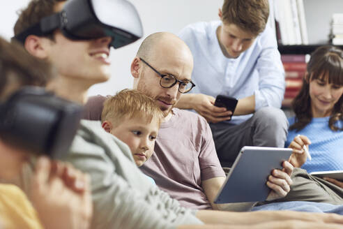 Glückliche Familie auf der Couch sitzend, mit VR-Brille und mobilen Geräten - MCF00228