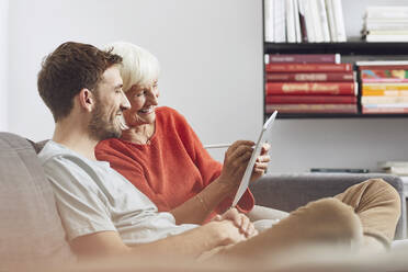 Enkel sitzt auf der Couch und benutzt mit seiner Großmutter ein digitales Tablet - MCF00252
