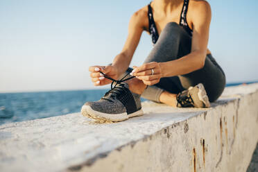 Sportlerin, die auf einer Mauer sitzt und einen Laufschuh bindet - OYF00030