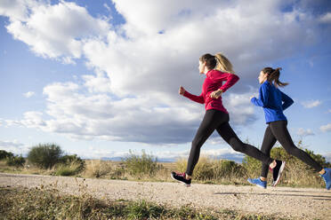 Young women running together in countryside - ABZF02536