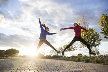 Young women having fun and jumping in park, against morning sun - ABZF02555