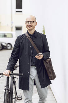 Mann mit Fahrrad auf dem Weg zur Arbeit, der sein Smartphone in der Hand hält - MCF00268