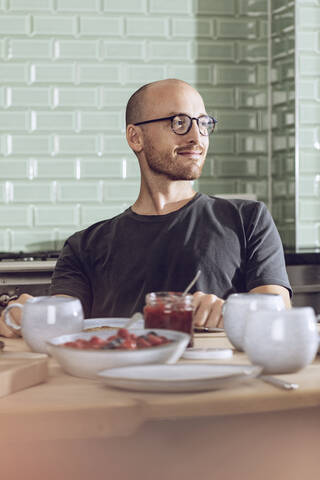 Lächelnder Mann sitzt am Frühstückstisch, lizenzfreies Stockfoto