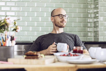 Mann hält eine Tasse am Frühstückstisch zu Hause - MCF00283