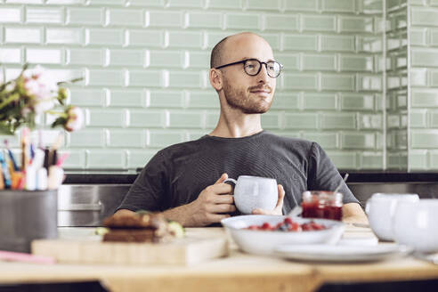 Mann hält eine Tasse am Frühstückstisch zu Hause - MCF00283