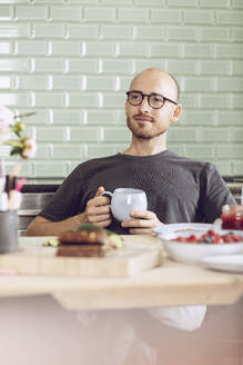 Mann hält eine Tasse am Frühstückstisch zu Hause - MCF00284