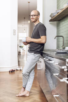 Mann mit einer Tasse morgens zu Hause in der Küche stehend - MCF00286