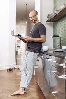 Mann, der morgens zu Hause in der Küche eine Zeitschrift liest - MCF00287