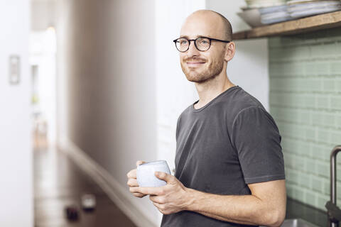 Mann mit einer Tasse morgens zu Hause in der Küche stehend, lizenzfreies Stockfoto
