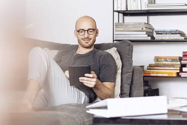 Mann sitzt zu Hause auf einer Couch und benutzt ein digitales Tablet - MCF00296