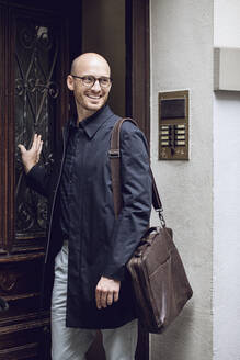 Lächelnder Mann auf dem Weg zur Arbeit vor der Eingangstür - MCF00312