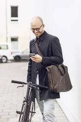 Mann mit Fahrrad auf dem Weg zur Arbeit schaut auf sein Smartphone - MCF00315