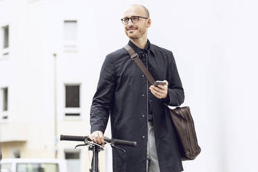 Man with bicycle going to work holding his smartphone - MCF00316