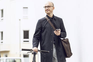 Mann mit Fahrrad auf dem Weg zur Arbeit, der sein Smartphone in der Hand hält - MCF00316