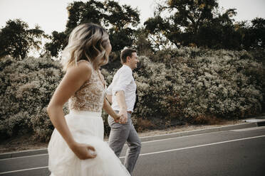 Bride and groom walking hand in hand on a country road - LHPF00754
