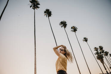 Low angle view of happy young woman under palm trees - LHPF00776