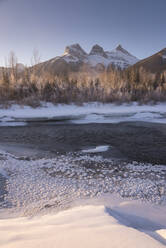 Winterlicher Sonnenaufgang mit gefrorenem Bow River und Three Sisters, Canmore, Alberta, Kanadische Rockies, Kanada, Nordamerika - RHPLF07152