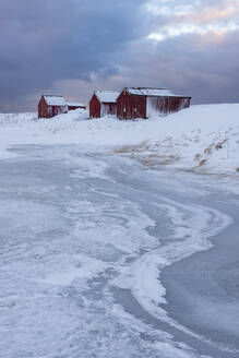 Fischerhäuser und Eisformationen mit dramatischem Himmel im Winter, Eggum, Lofoten, Arktis, Norwegen, Europa - RHPLF07389