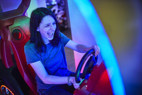 Aufgeregte Frau, die mit einem Fahrsimulator in einer Spielhalle spielt und Spaß hat - ZEDF02585