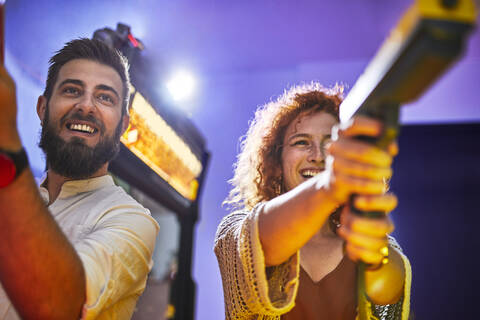 Glückliches Paar spielt und schießt mit Pistolen in einer Spielhalle, lizenzfreies Stockfoto