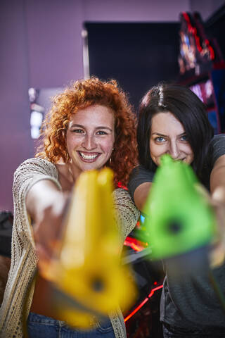 Glückliche Freunde spielen und schießen mit Pistolen in einer Spielhalle, lizenzfreies Stockfoto
