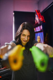 Porträt einer lächelnden Frau, die in einer Spielhalle mit Pistolen schießt - ZEDF02602