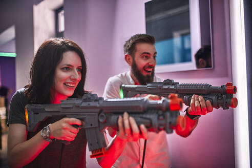 Glückliches Paar spielt und schießt mit Gewehren in einer Spielhalle - ZEDF02606
