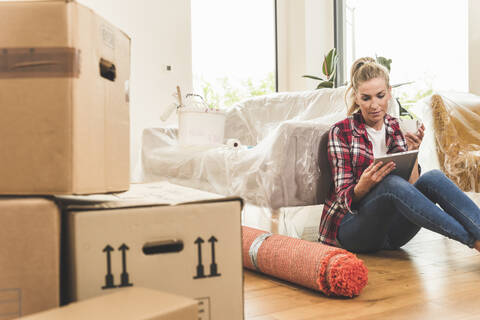 Woman sitting on the floor in new home using tablet stock photo