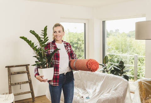 Frau zieht mit Teppich und Topfpflanze in ein neues Haus ein, lizenzfreies Stockfoto