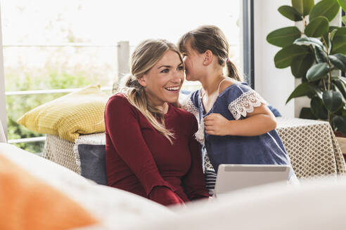 Girl whispering into mother's ear at home - UUF18888