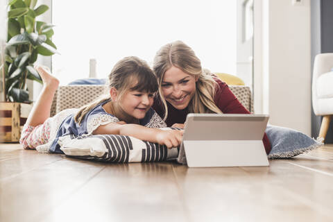Mutter und Tochter liegen zu Hause auf dem Boden und benutzen ein Tablet, lizenzfreies Stockfoto