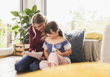 Mother helping daughter with homework at home - UUF18894