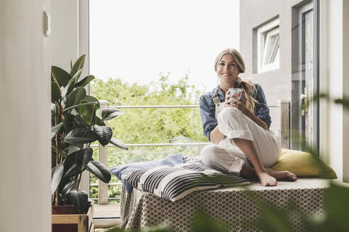 Porträt einer Frau, die zu Hause am Fenster sitzt und eine Kaffeepause macht - UUF18930