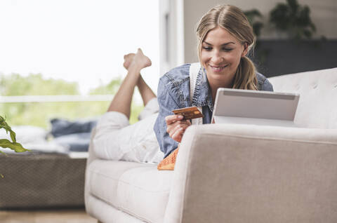 Lächelnde Frau auf Couch mit Kreditkarte und Tablet, lizenzfreies Stockfoto