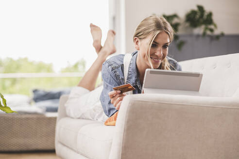 Lächelnde Frau auf Couch mit Kreditkarte und Tablet - UUF18945
