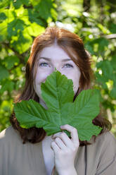 Female teenager in a forest holding a leaf in front of her mouth - LBF02679