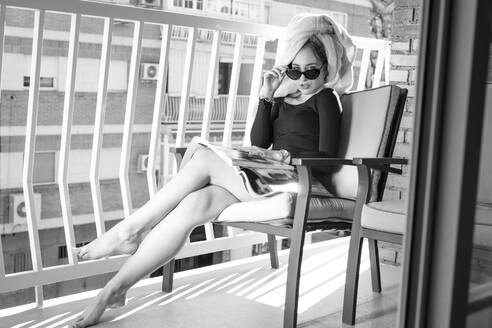 Glamour lady reading a magazine on balcony, hand on glasses - LJF00876