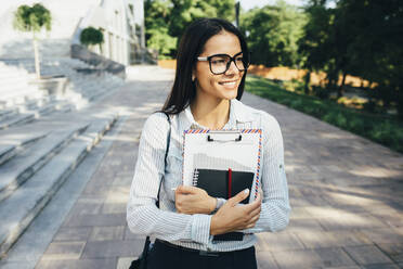 Smiling young woman walking with papers outdoors - OYF00039
