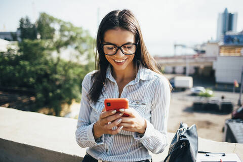 Smiling young businesswoman checking cell phone outdoors stock photo