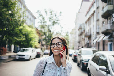 Glückliche junge Geschäftsfrau im Gespräch mit Handy auf der Straße - OYF00048