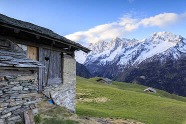 Alphütte umrahmt von Wiesen und verschneiten Gipfeln in der Morgendämmerung, Tombal, Soglio, Bergell, Kanton Graubünden, Schweiz, Europa - RHPLF07458