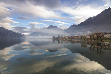 Berge und Dorf spiegeln sich im nebelverhangenen Mezzola-See in der Morgendämmerung, Verceia, Chiavenna-Tal, Lombardei, Italien, Europa - RHPLF07473