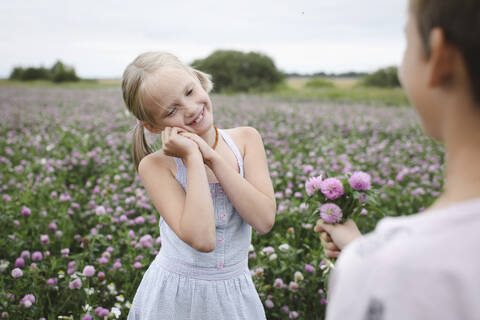 Junge schenkt einem lächelnden Mädchen eine Kleeblume, lizenzfreies Stockfoto