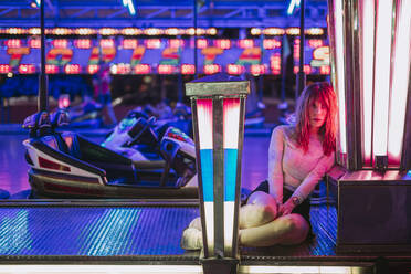 Junge Frau sitzt im Autoscooter auf einem Jahrmarkt bei Nacht - LJF00881