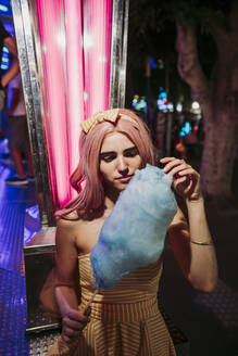 Porträt einer jungen Frau mit Zuckerwatte auf einem Jahrmarkt bei Nacht - LJF00900