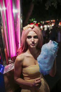 Porträt einer jungen Frau mit Zuckerwatte auf einem Jahrmarkt bei Nacht - LJF00901