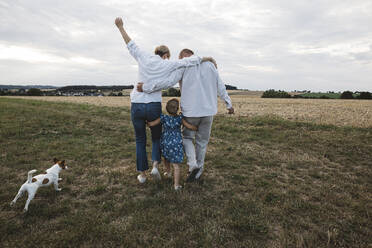 Rear view of family with dog walking on a meadow - KMKF01052