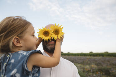 Tochter bedeckt Augen des Vaters mit Sonnenblumen - KMKF01055