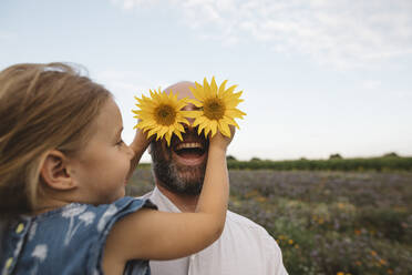 Tochter bedeckt Augen des Vaters mit Sonnenblumen - KMKF01056